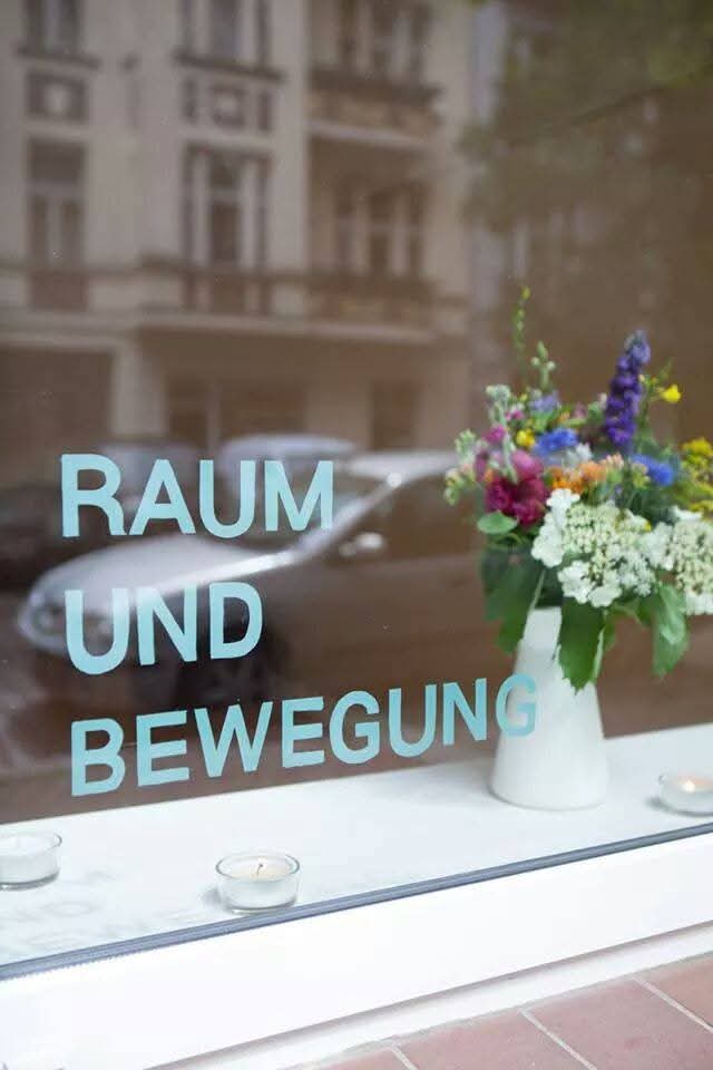 Blick durch das Fenster auf Kerzen und Blumen.
